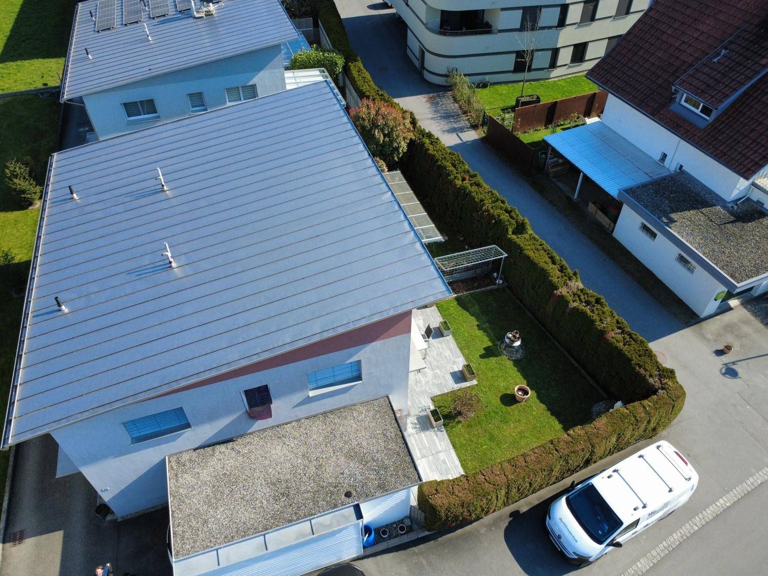 Draufsicht auf das Wohnhaus mit modernem Dach, gepflegtem Garten und angrenzender Straße.