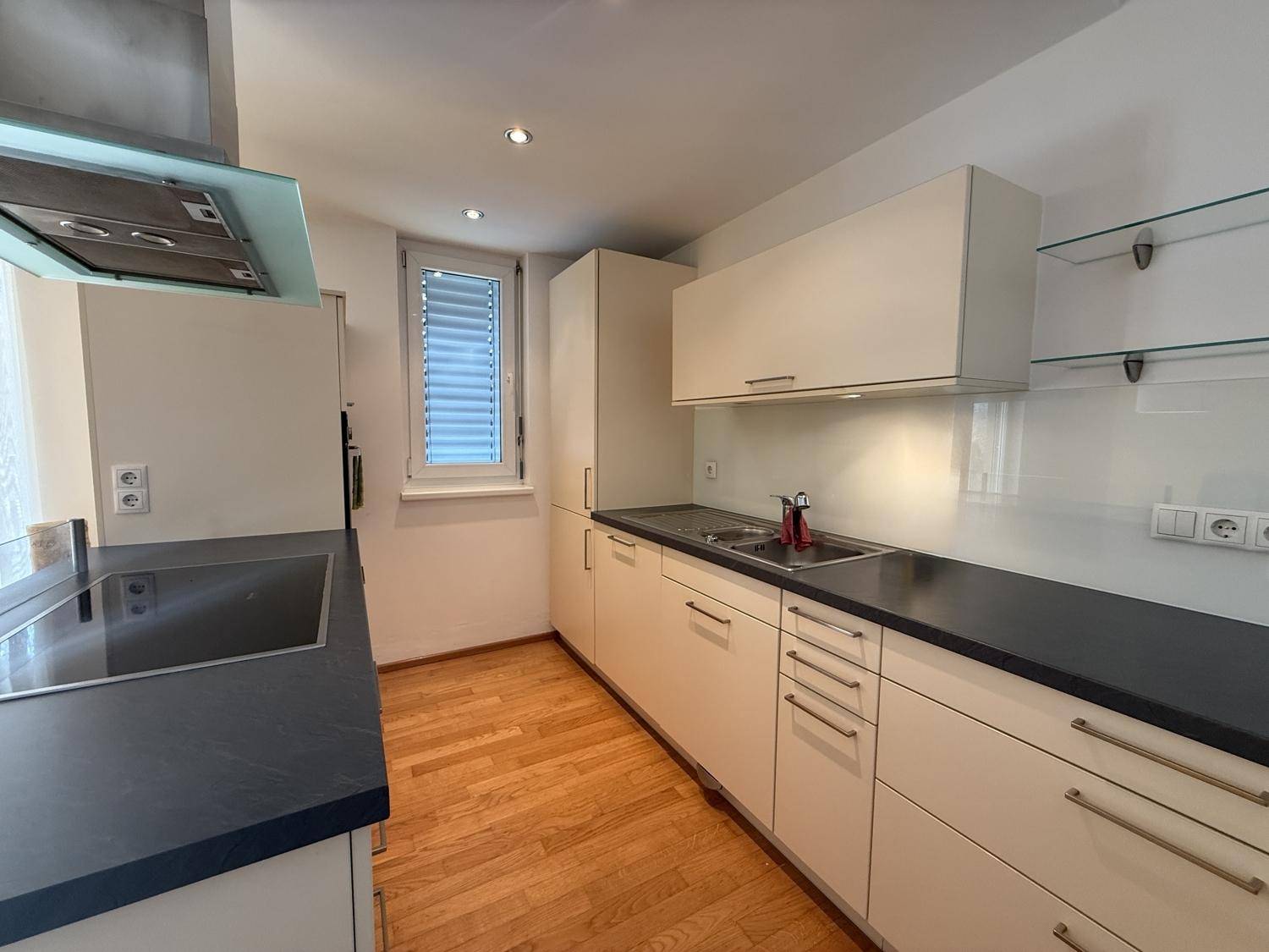 Moderne Küche mit hellen Schränken, dunkler Arbeitsplatte und Induktionskochfeld.