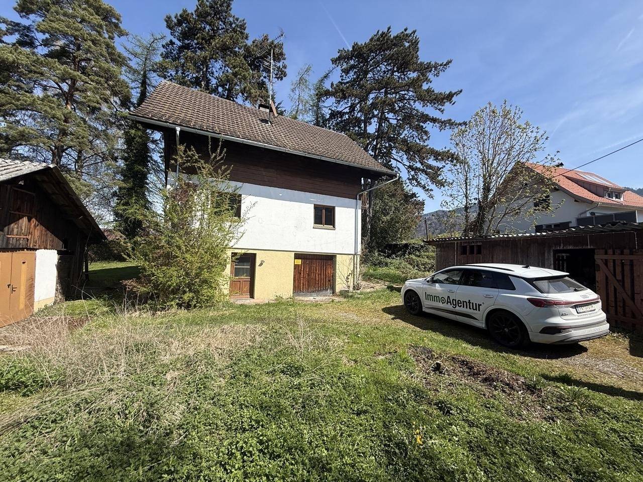 Ansicht des Hauses mit Schuppen und Fahrzeug auf dem Grundstück an einem sonnigen Tag.