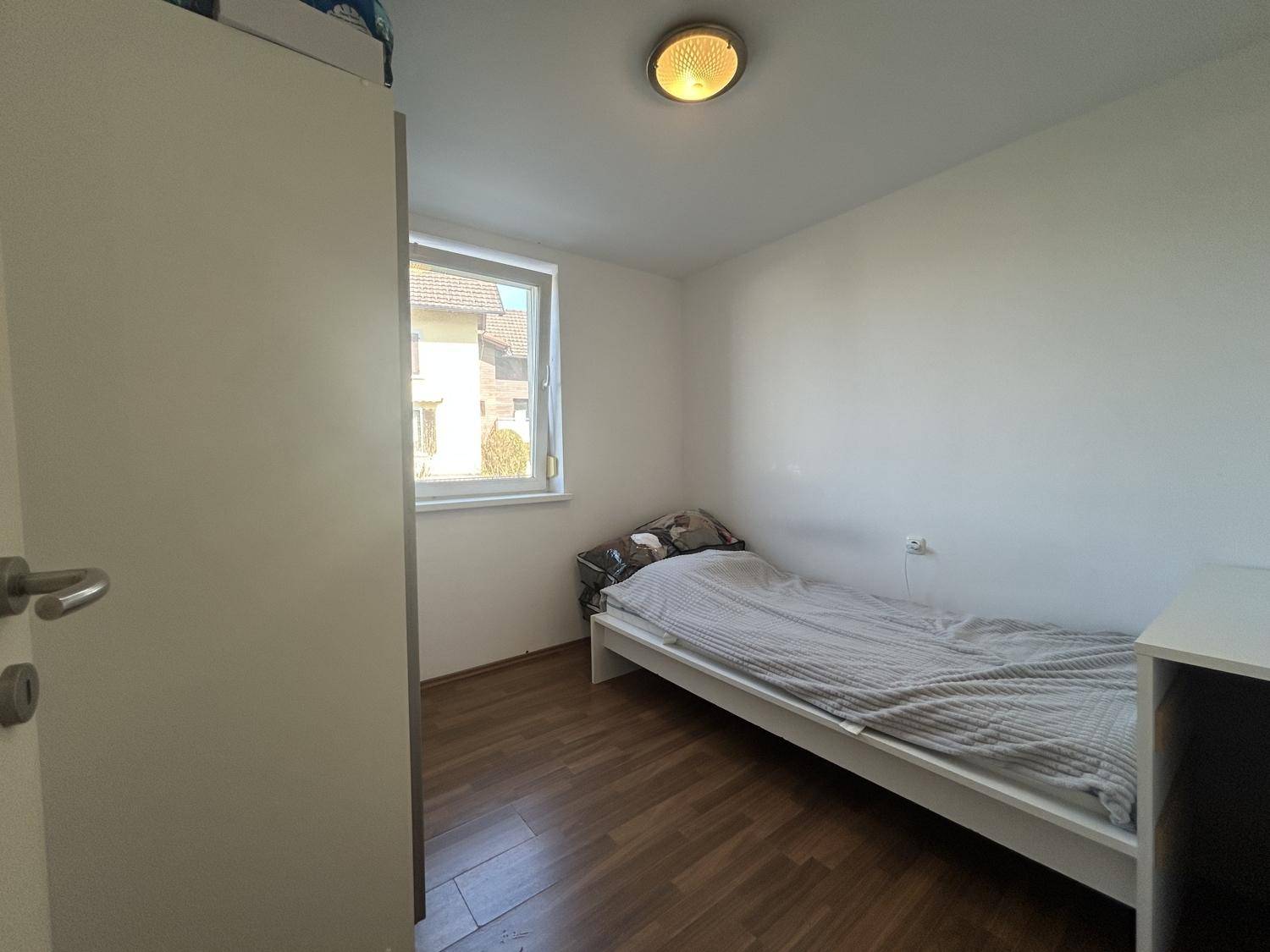 Kleines Schlafzimmer mit Einzelbett, Fenster und Laminatboden, ideal als Kinder- oder Gästezimmer.
