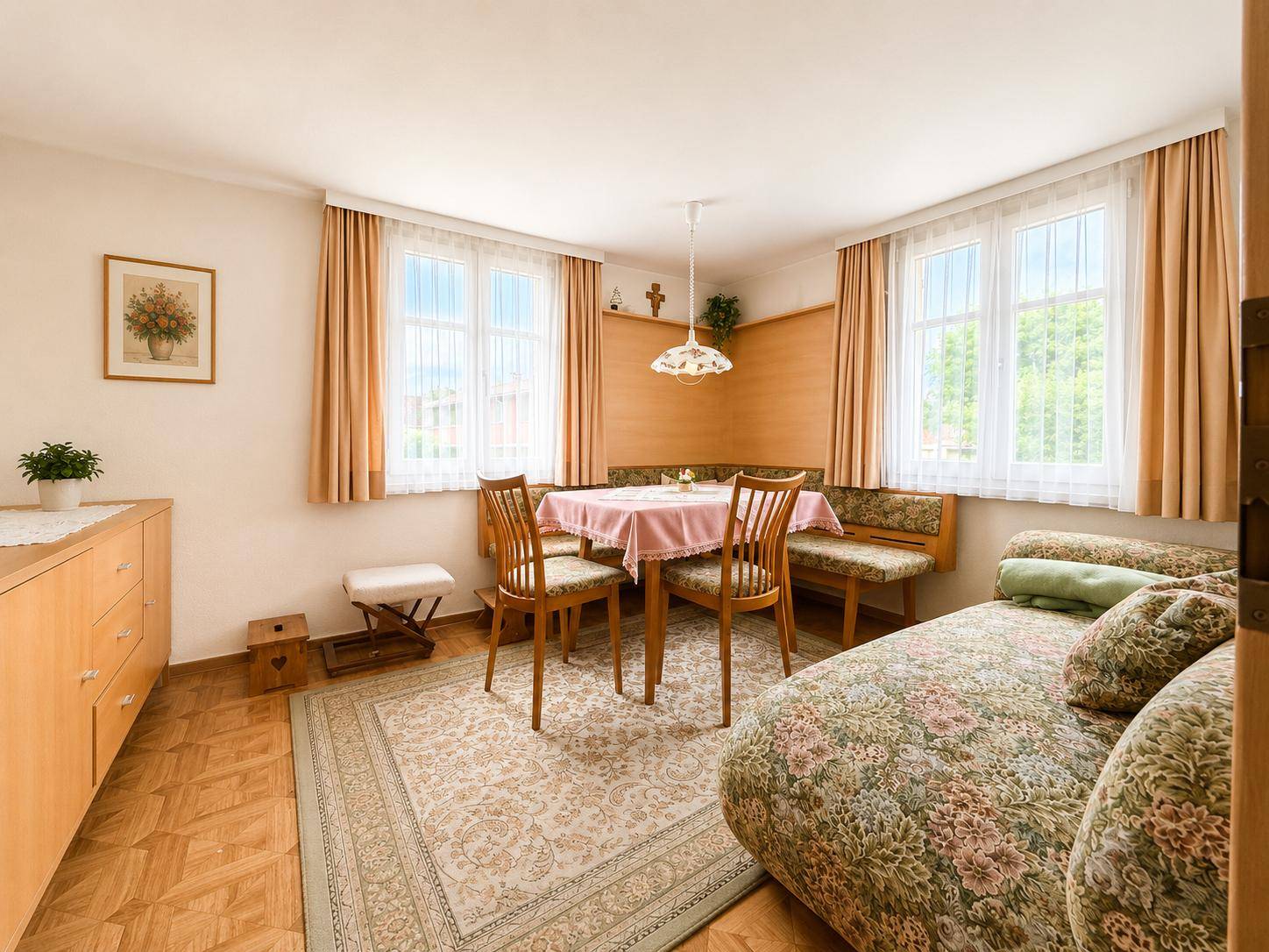 Gemütlicher Essbereich mit Holzmöbeln, floralem Sofa und Teppichboden.