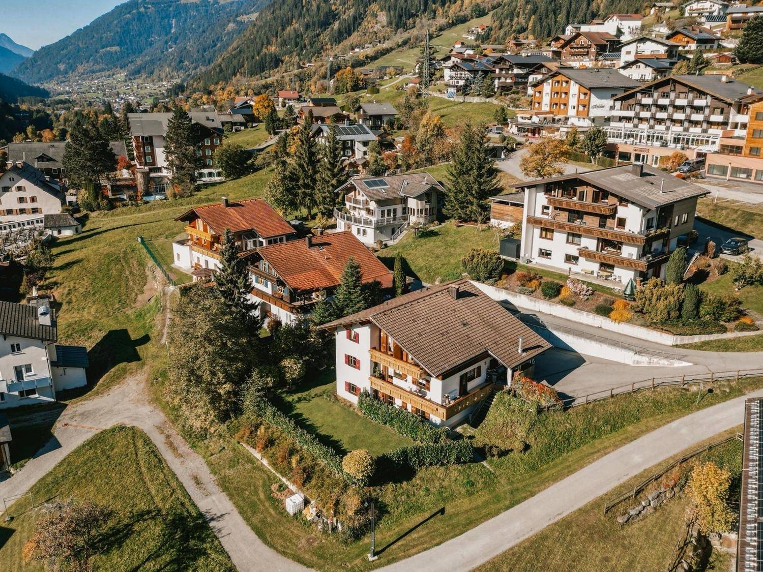 Luftaufnahme eines idyllischen Bergdorfes mit vielen Häusern und herbstlicher Landschaft.