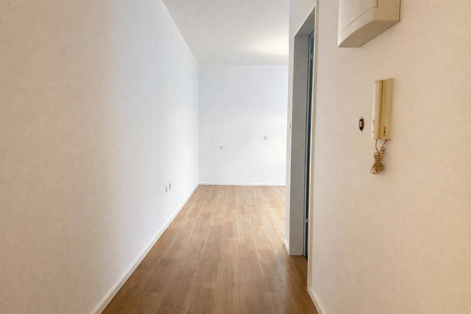 Heller Flur mit Laminatboden und Gegensprechanlage, der zu weiteren Räumen führt.