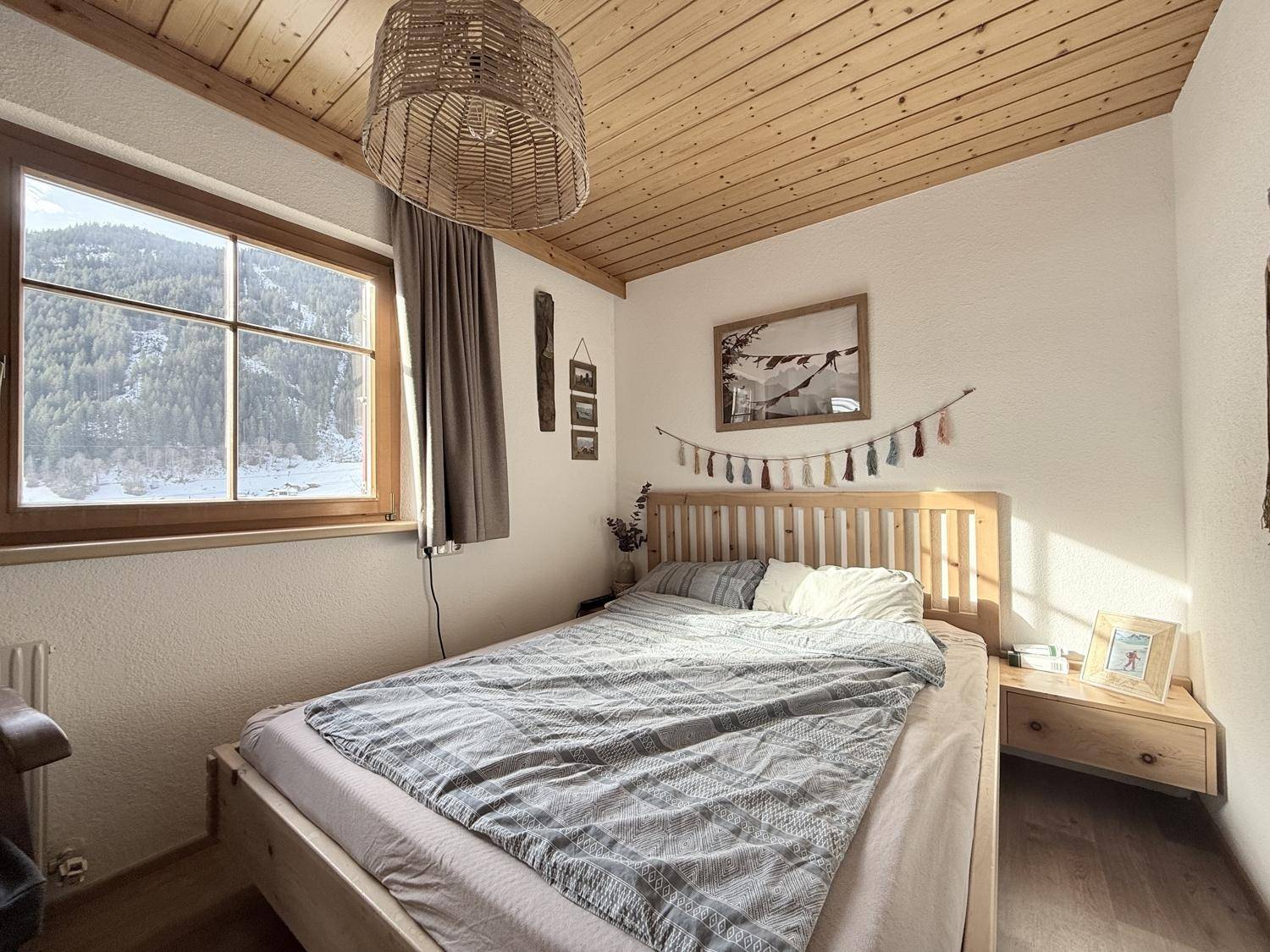 Helles Schlafzimmer mit Holzwänden, Doppelbett und Fenster mit Blick auf die verschneiten Berge.