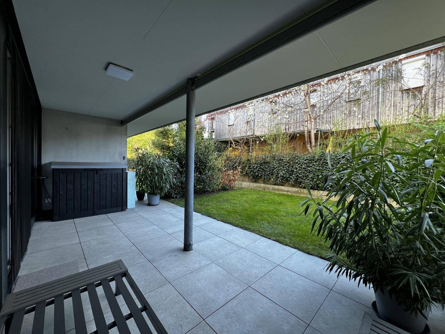 Überdachte Terrasse mit Fliesenboden, Gartenmöbeln und Blick ins Grüne.