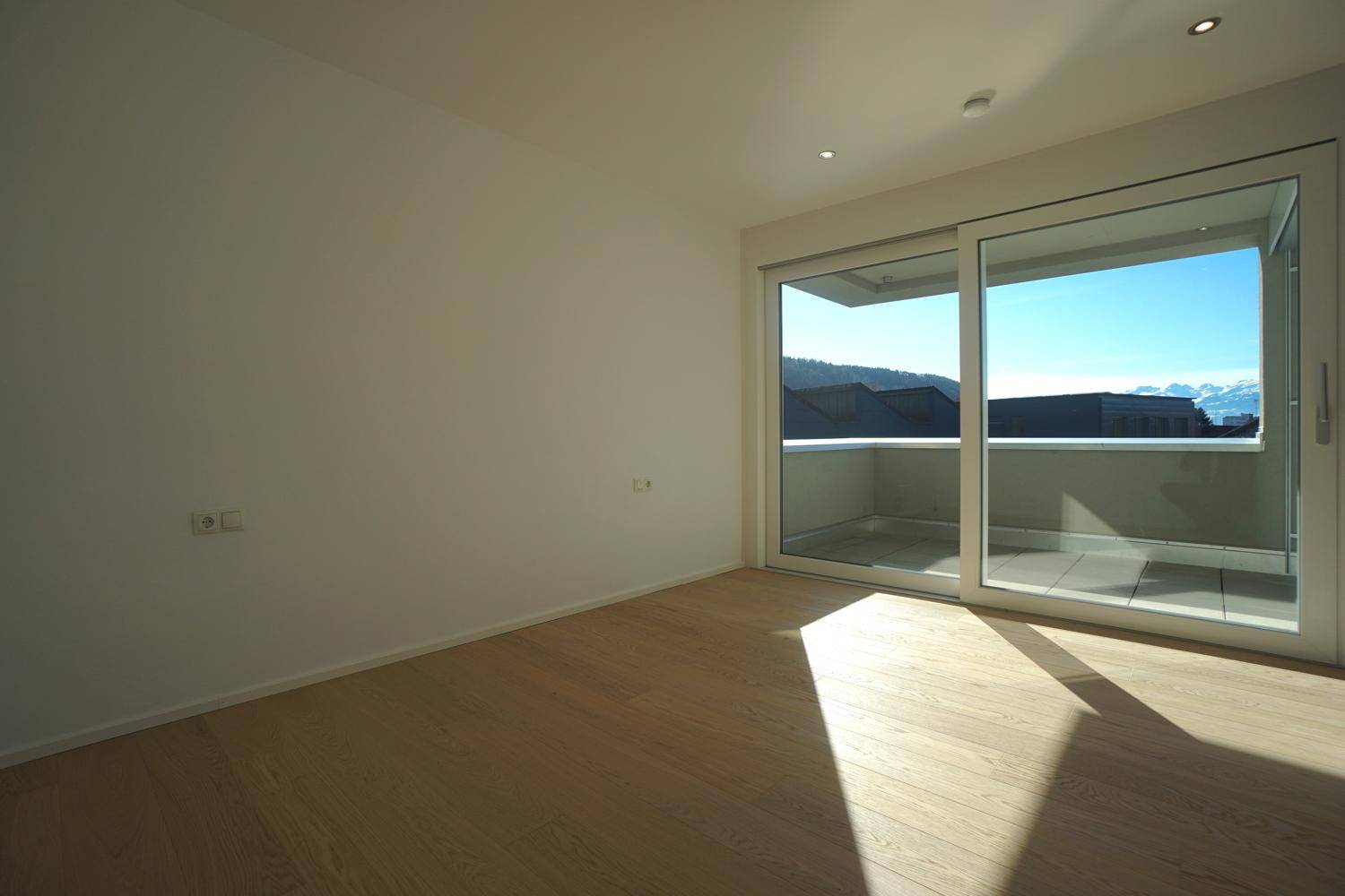Heller Wohnraum mit Holzboden und großzügigen Schiebetüren, die Zugang zum Balkon ermöglichen.