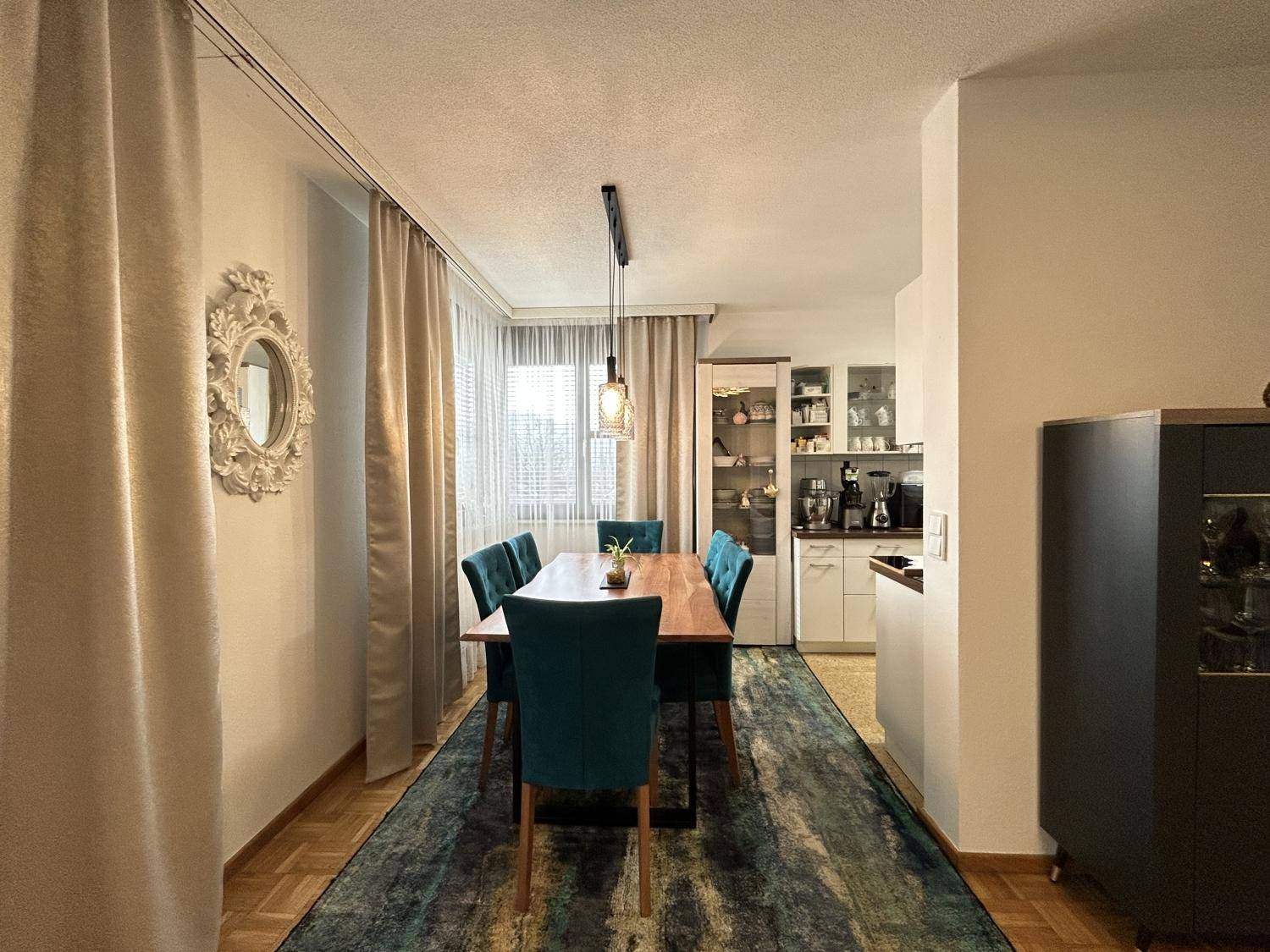 Heller Essbereich mit Holztisch und blauen Stühlen, angrenzend an eine moderne Küche.