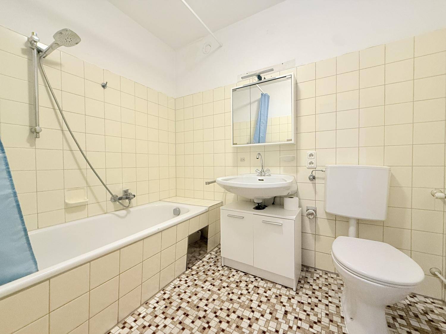 Badezimmer mit gelben Wandfliesen, Badewanne mit Duschfunktion, WC und Waschbecken mit Spiegelschrank.