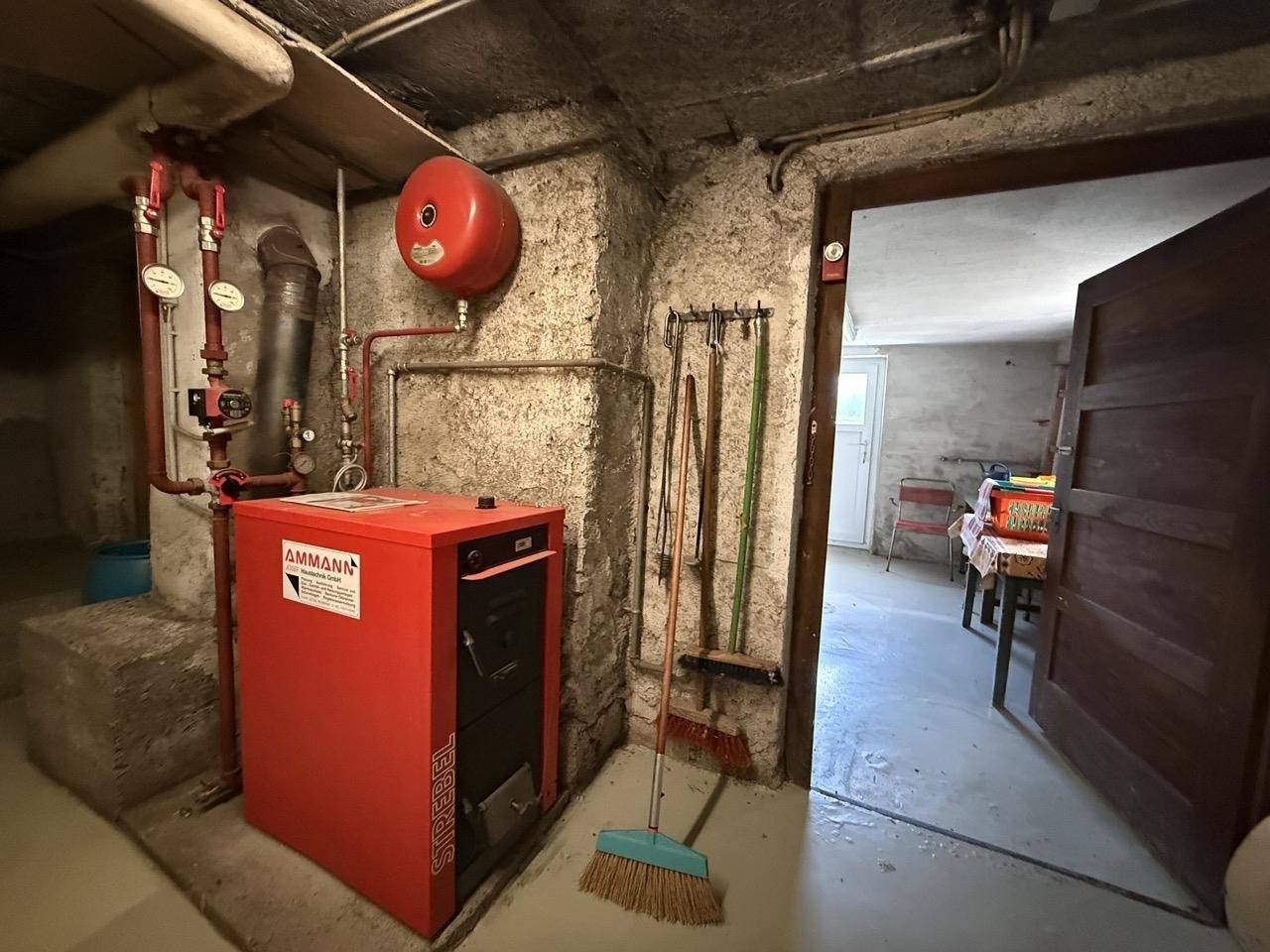 Heizungsraum im Keller mit rotem Heizkessel und sichtbaren Rohren.