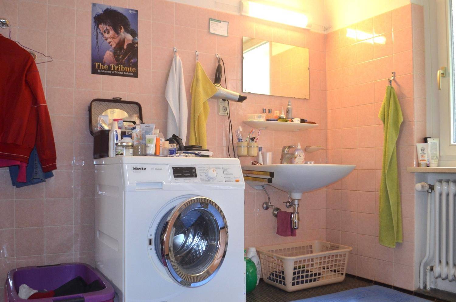 Badezimmer mit rosa Fliesen, Waschbecken und einer Waschmaschine.