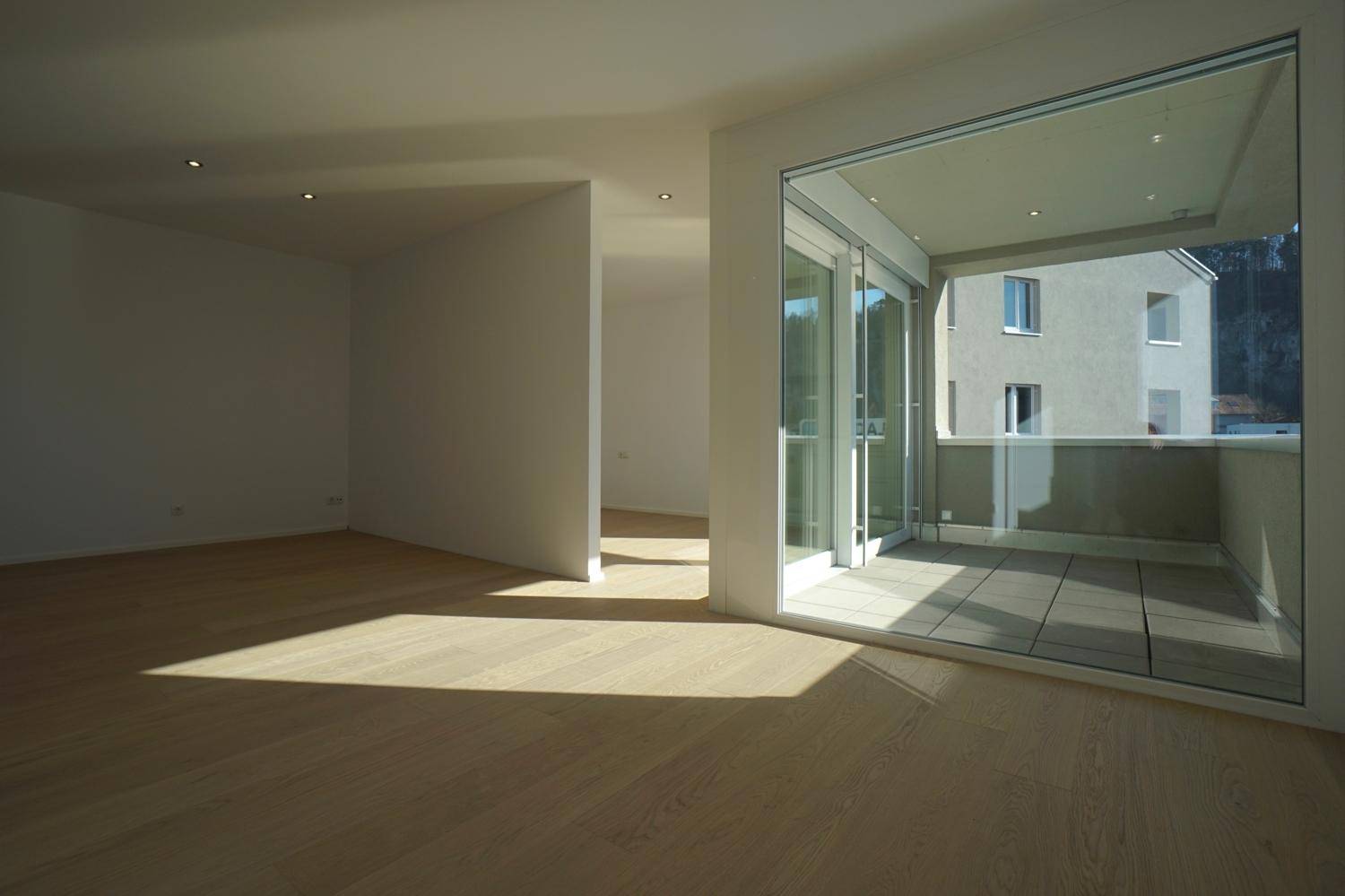 Lichtdurchfluteter Wohnbereich mit hellem Holzboden und Schiebetüren zum Balkon.