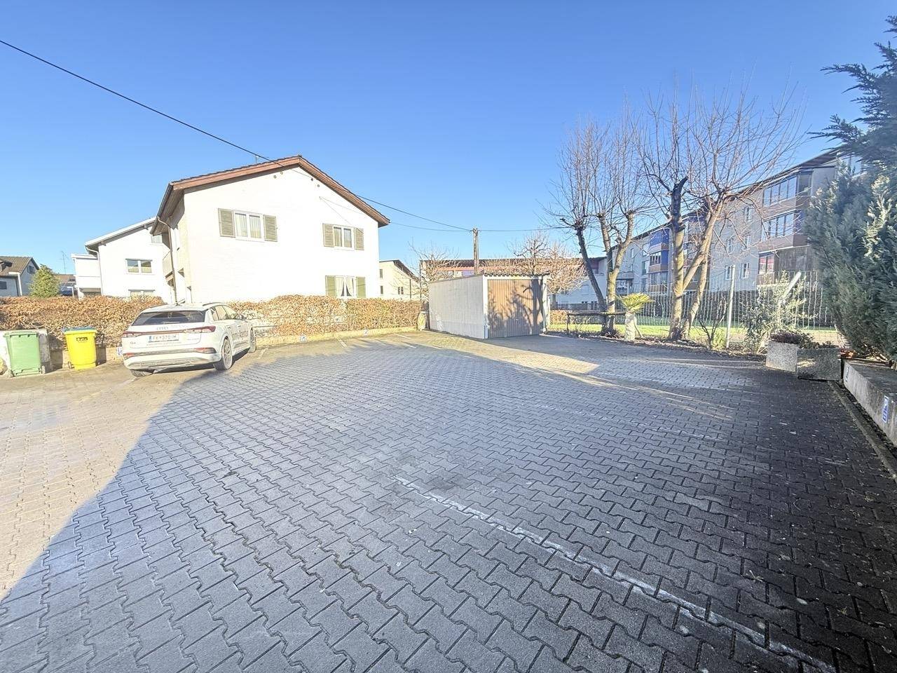 Großer gepflasterter Parkplatz mit einem Auto und umgebender Vegetation.