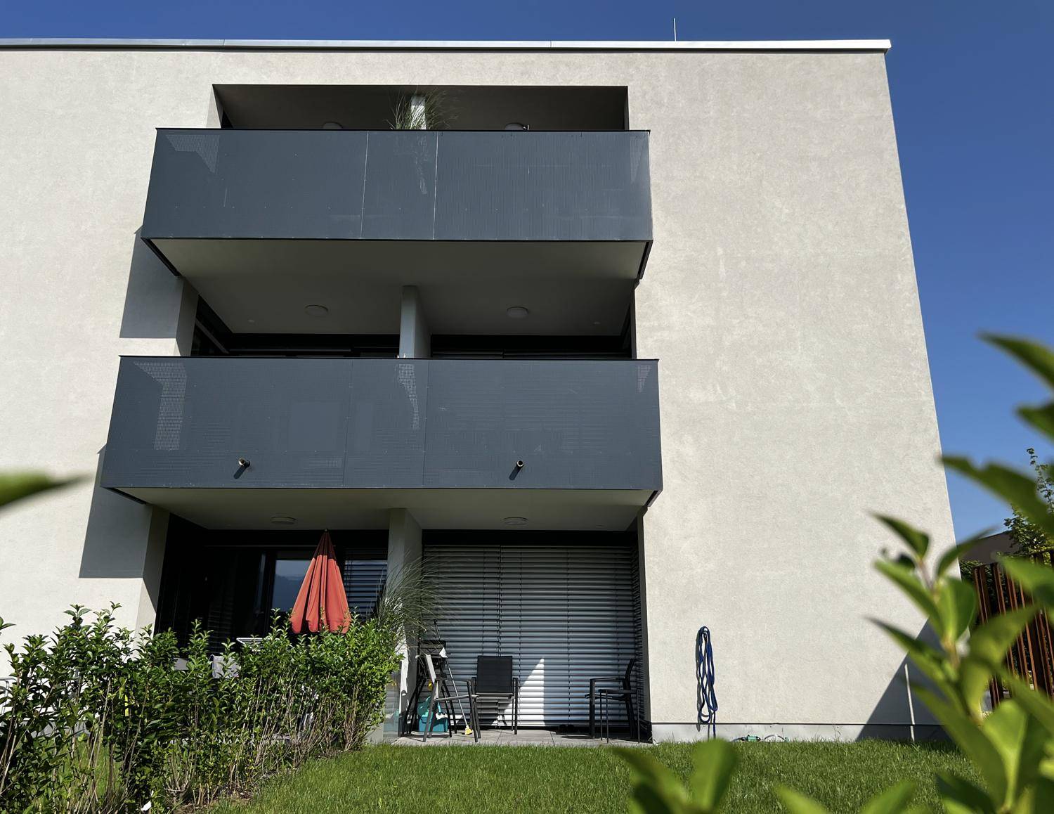 Nahaufnahme der modernen Balkone und der Terrasse im Erdgeschoss mit Sonnenschirm.