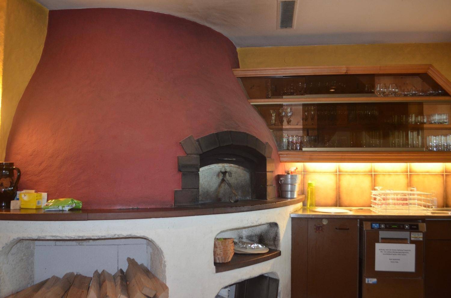 Detailansicht eines großen, traditionellen Steinofens mit Holzablage in der Küche.