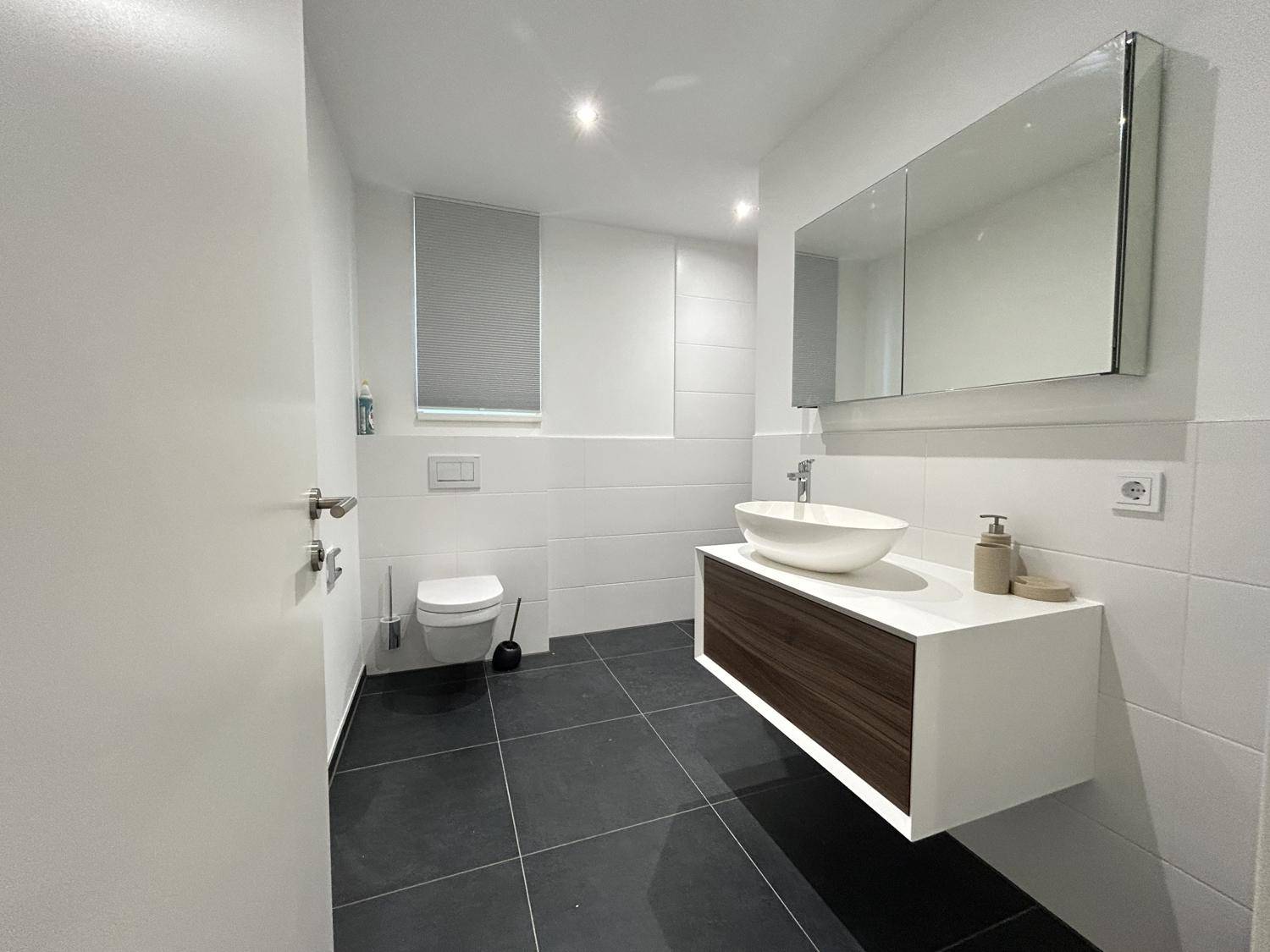 Modernes Badezimmer mit dunklen Fliesen, schwebendem Waschtisch und Wand-WC.