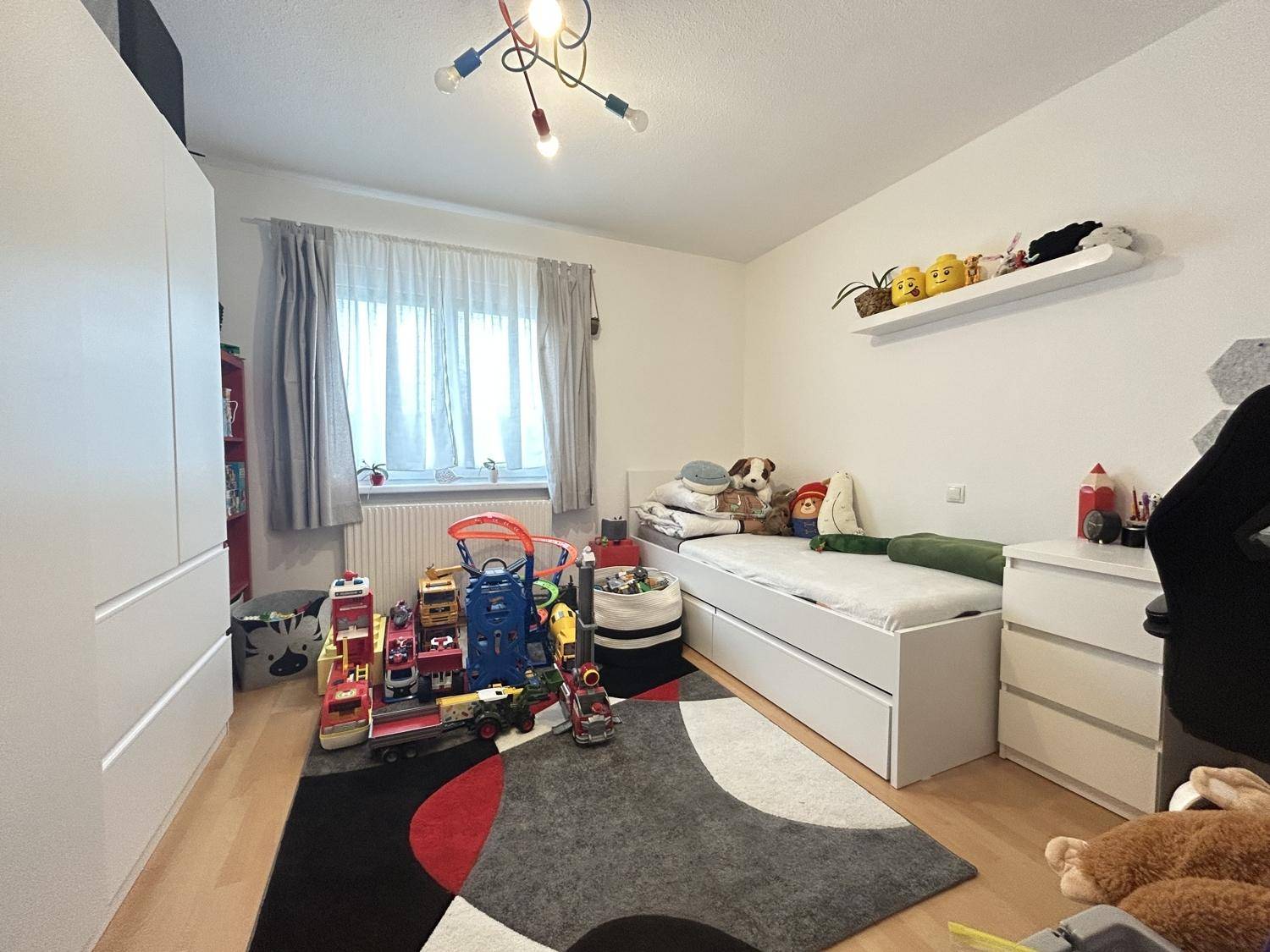 Kinderzimmer mit Einzelbett, Spielzeug und weißem Kleiderschrank, ideal für junge Bewohner.
