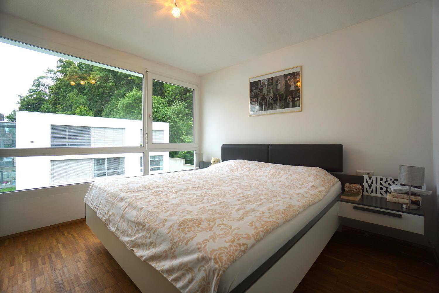 Helles Schlafzimmer mit Doppelbett, Nachttischen und großem Fenster mit Blick ins Grüne.