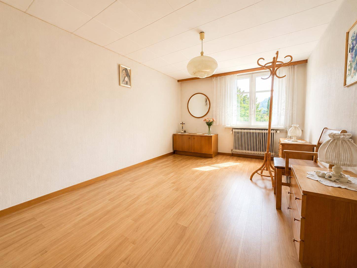 Helles Schlafzimmer mit Holzfußboden, schlichter Einrichtung und Fensterblick.