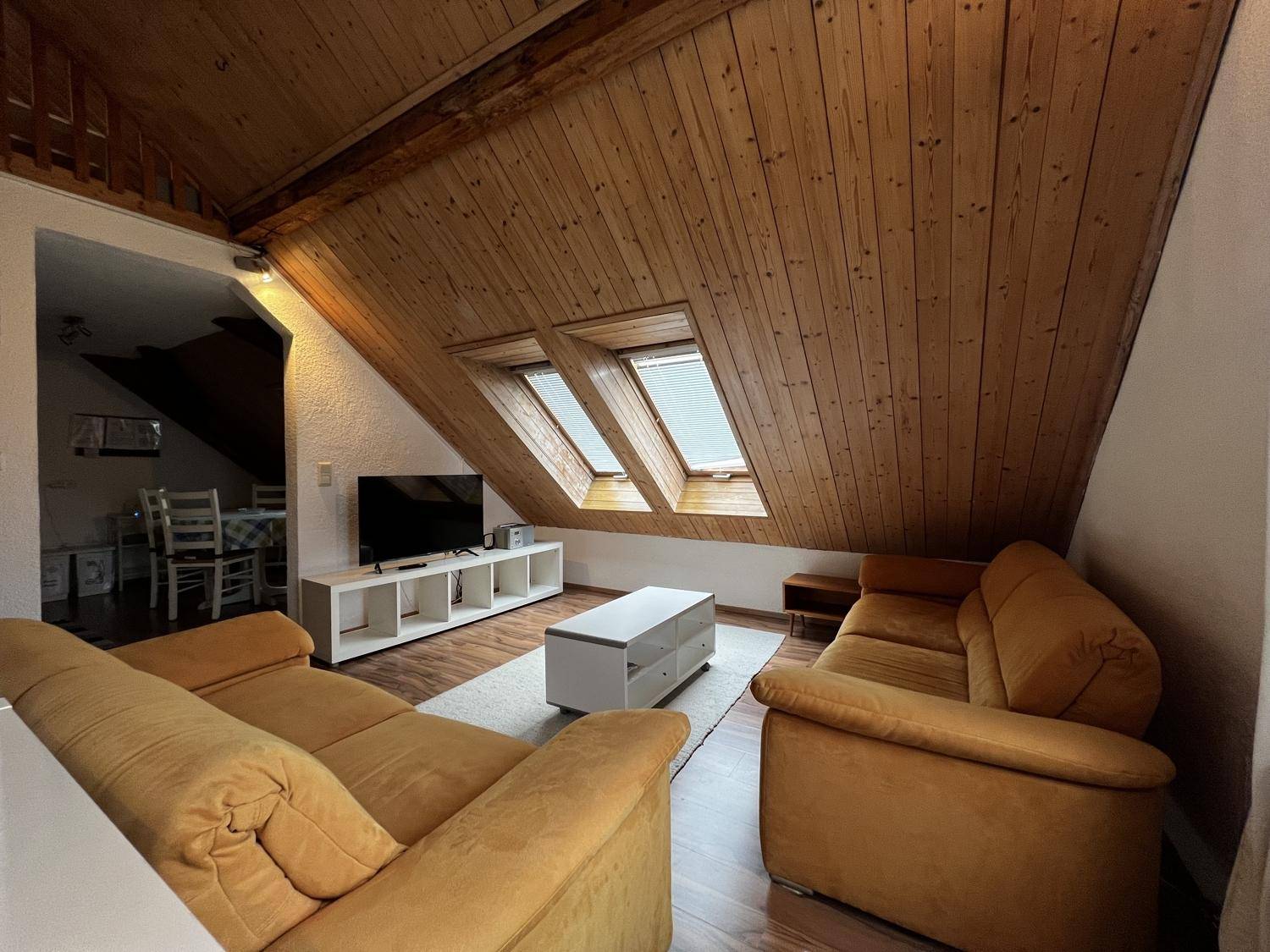 Gemütliches Wohnzimmer im Dachgeschoss mit bequemen Sofas, Holztäfelung und Dachfenstern.