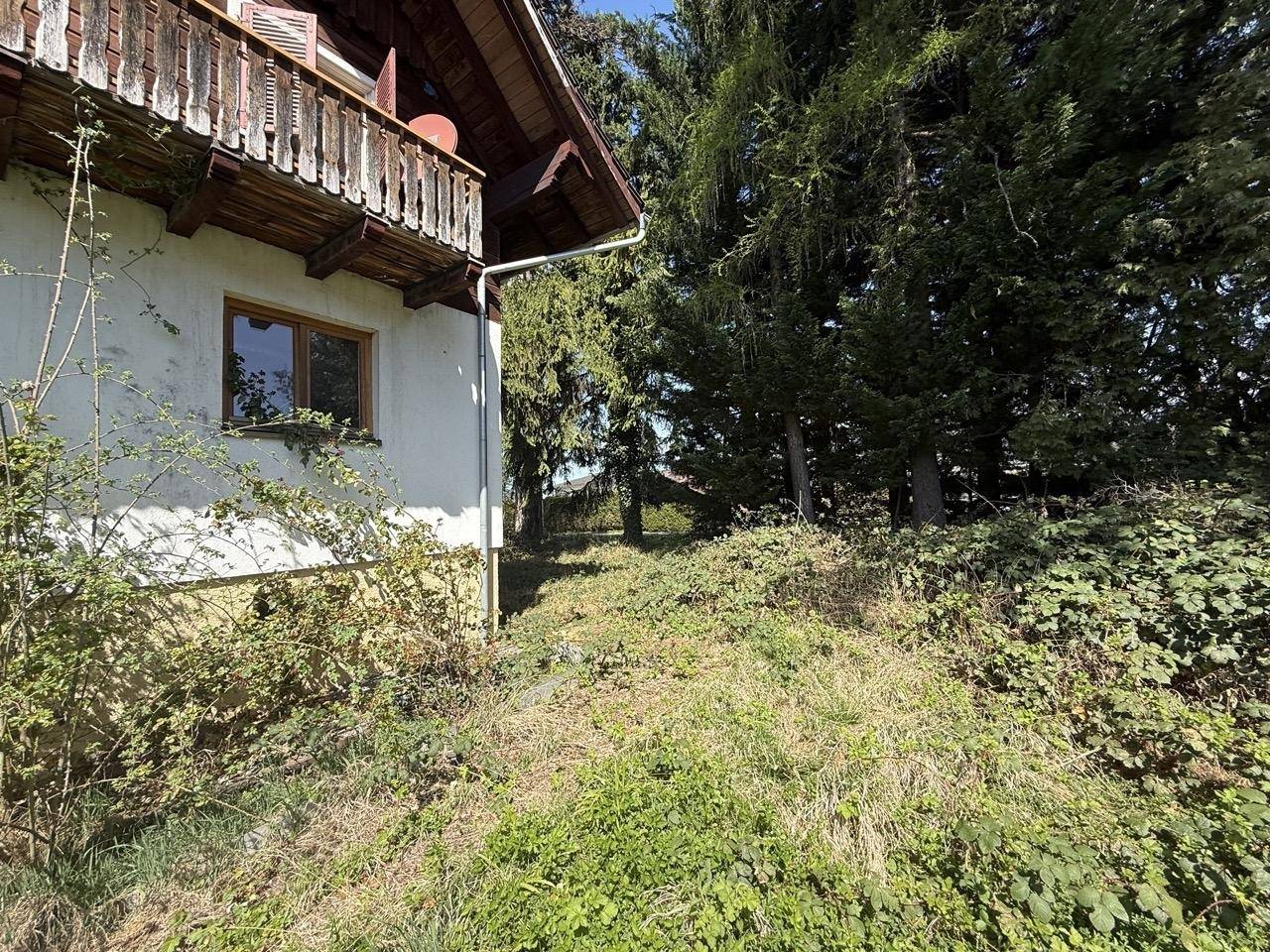 Seitenansicht des Hauses mit Balkon und einem Hanggrundstück mit dichter Vegetation.