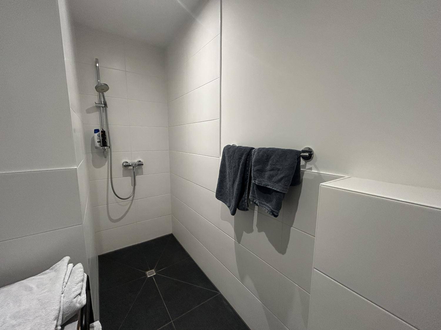 Begehbare Dusche mit dunklen Bodenfliesen und weiß gefliesten Wänden.