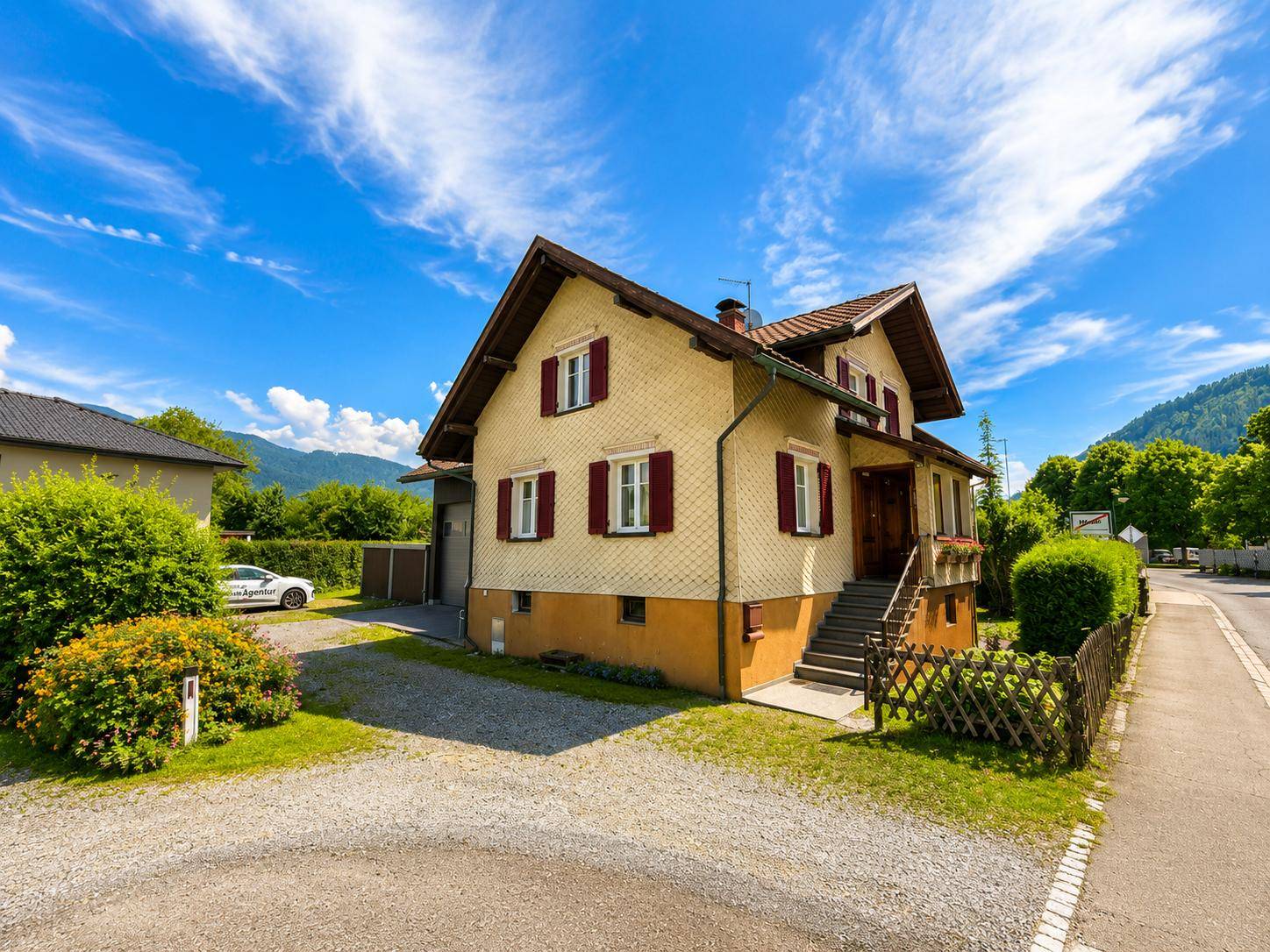 Seitenansicht des Hauses mit gelber Fassade, roten Fensterläden und Blick auf die Berge.