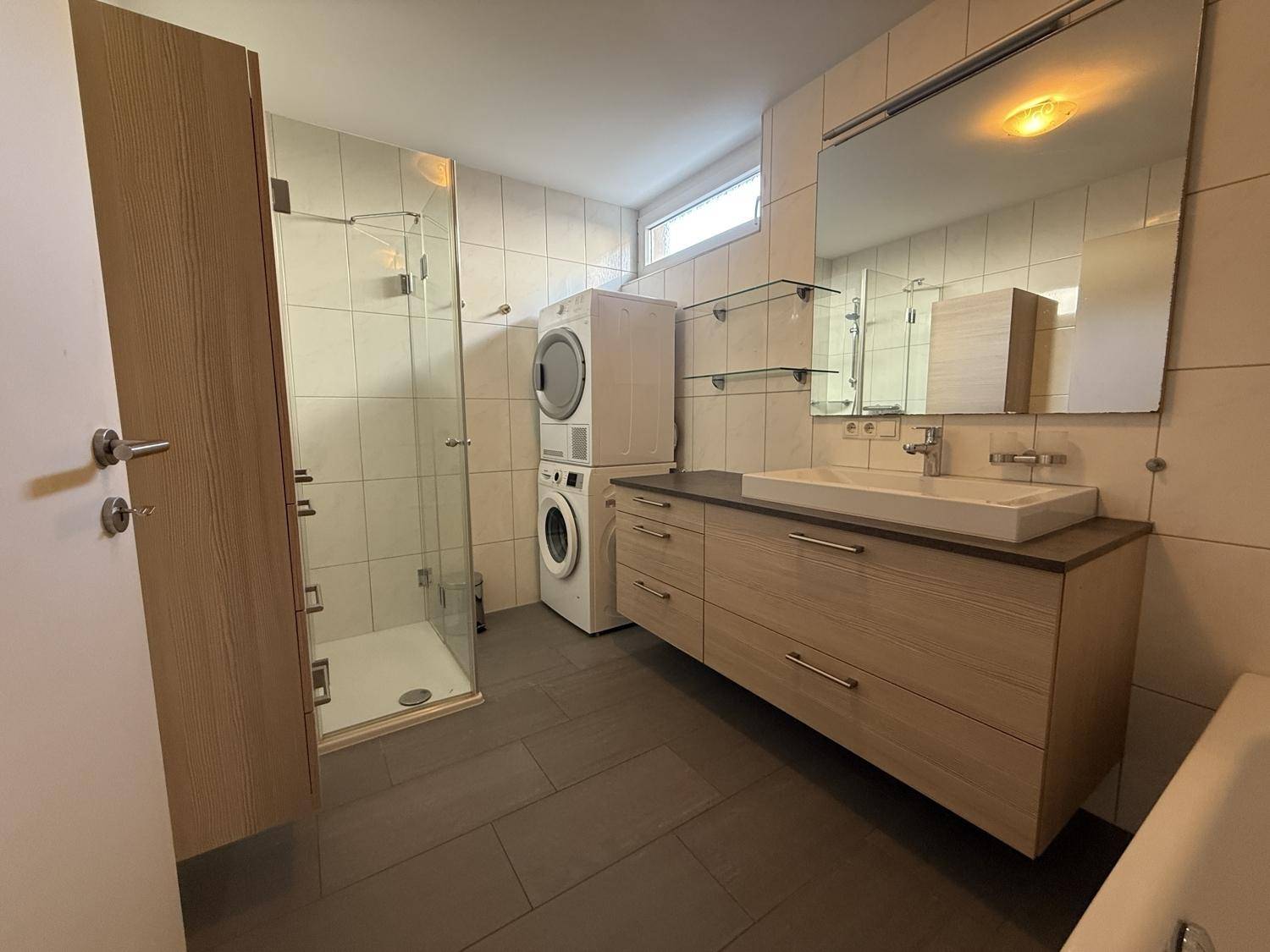 Modernes Badezimmer mit Dusche, großem Waschtisch und integrierten Waschmaschinen/Trockner.