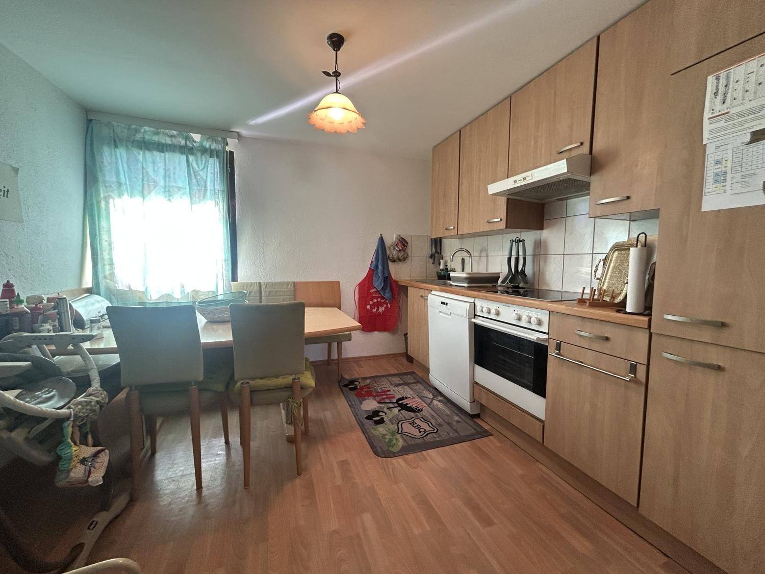 Funktionale Küche mit Holzschränken, Essbereich und Fenster, ausgestattet mit grundlegenden Geräten.