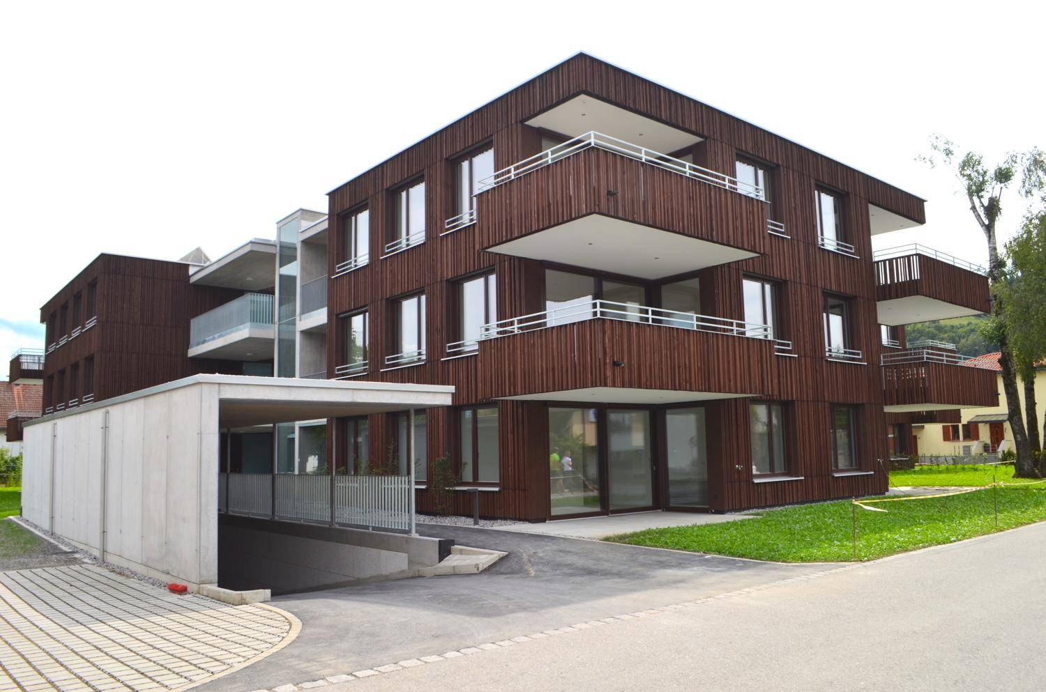 Modernes Wohngebäude mit Holzverkleidung, großen Fenstern und Balkonen sowie Zugang zur Tiefgarage.
