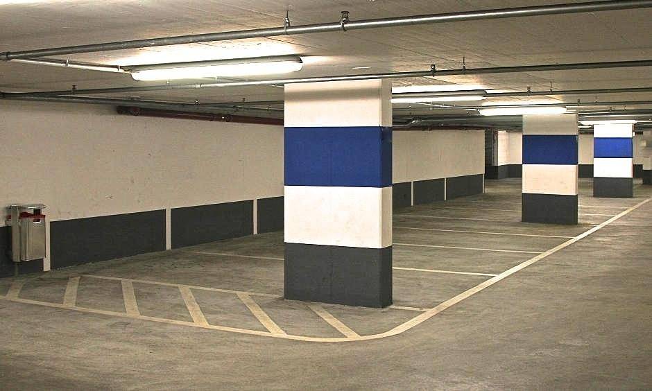 Leere Tiefgarage mit markierten Stellplätzen, Betonboden und Säulen in Weiß, Blau und Grau.