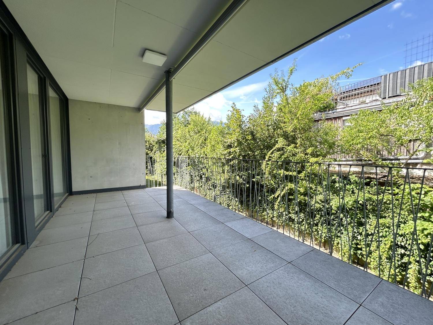 Geräumiger überdachter Balkon mit Fliesenboden und Blick ins Grüne.