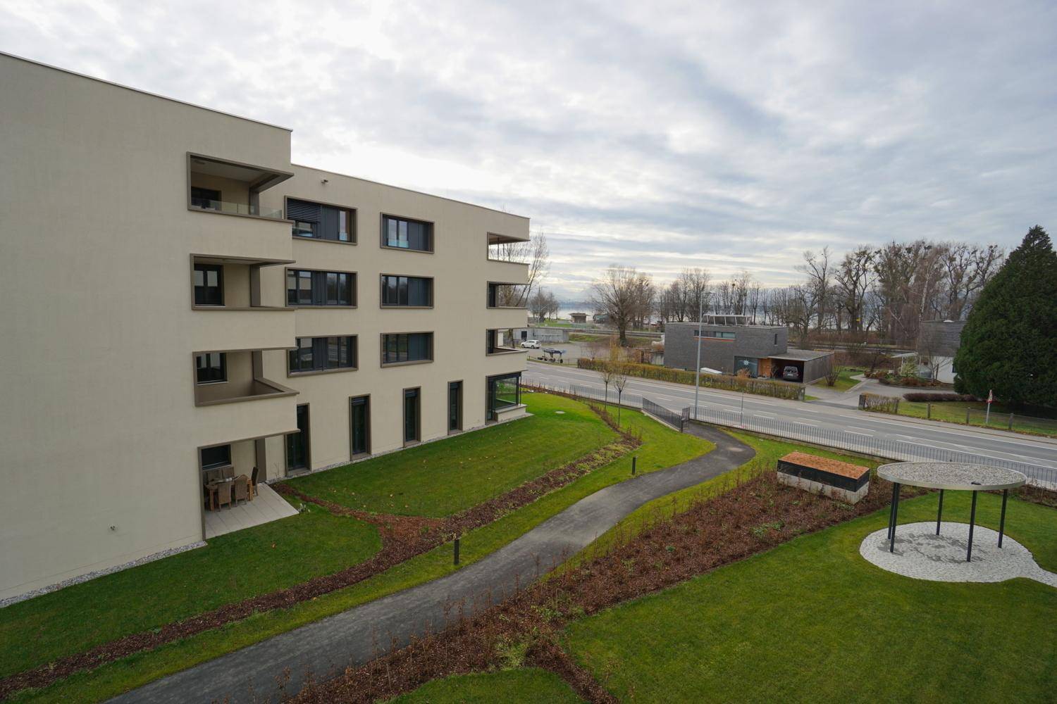 Gebäudekomplex mit gepflegten Grünflächen und Blick auf den See und die Landschaft.