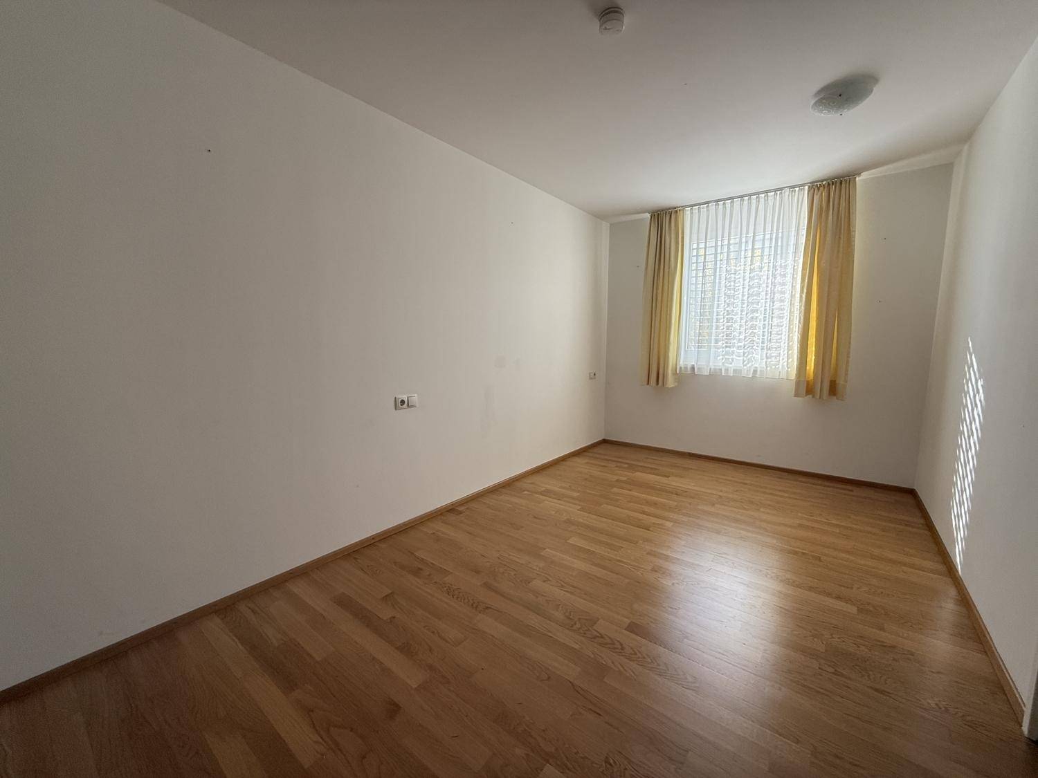 Helles, leeres Zimmer mit Holzboden und Fenster, vielseitig nutzbar als Schlaf- oder Arbeitszimmer.