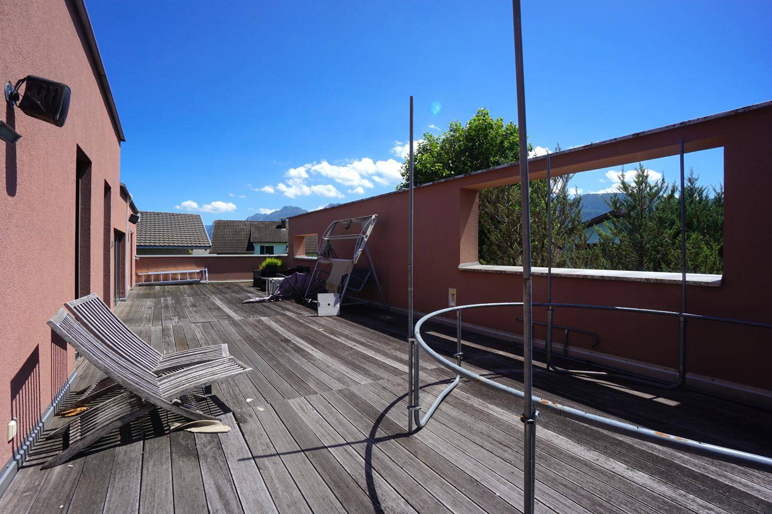 Geräumige Dachterrasse mit Holzbelag, Liegestühlen und weitem Blick auf die umliegende Landschaft und Berge.
