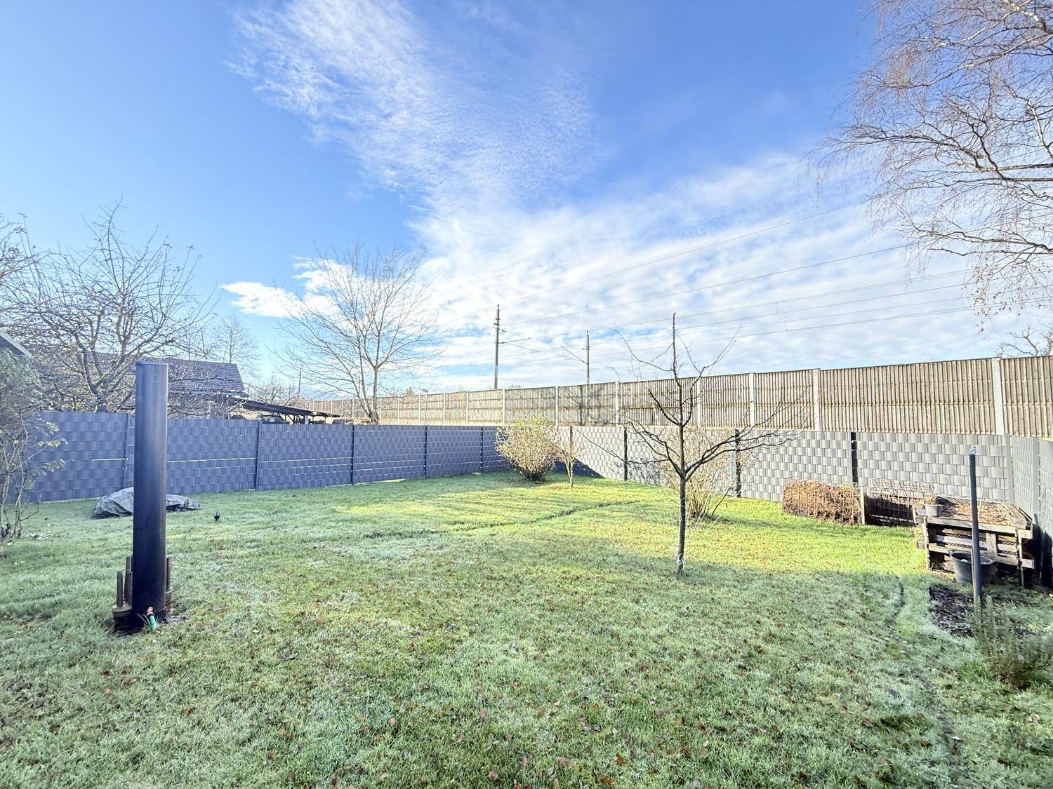 Gepflegter Garten mit Rasenfläche und Zaun unter blauem Himmel.