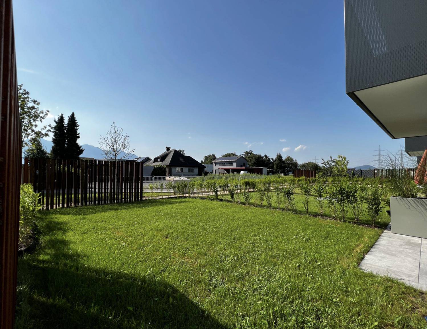 Gepflegter Rasenbereich neben dem Gebäude mit Hecke und Blick auf die ländliche Umgebung.