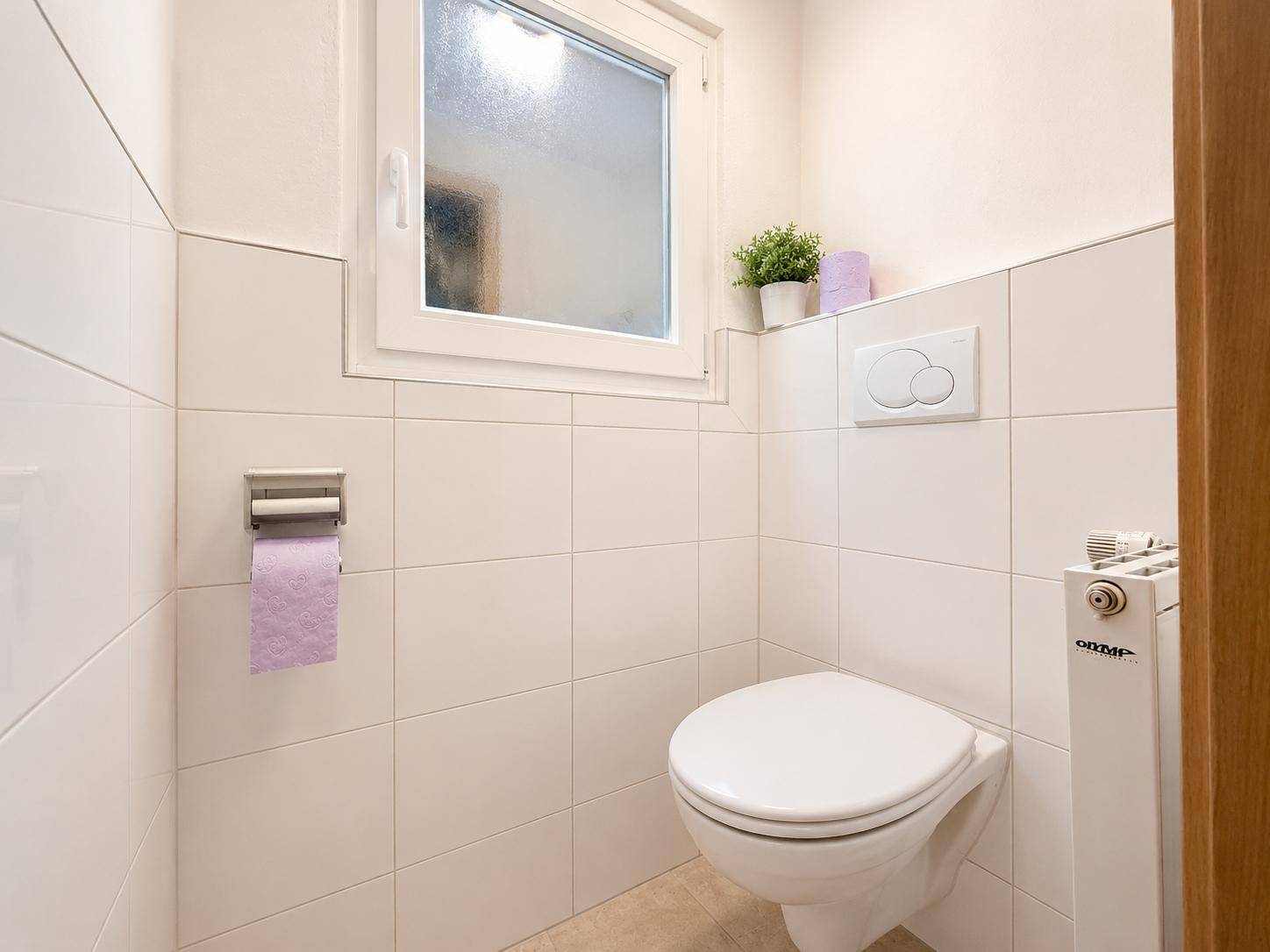 Kleines Gäste-WC mit weißen Fliesen, wandhängendem WC und Fenster.