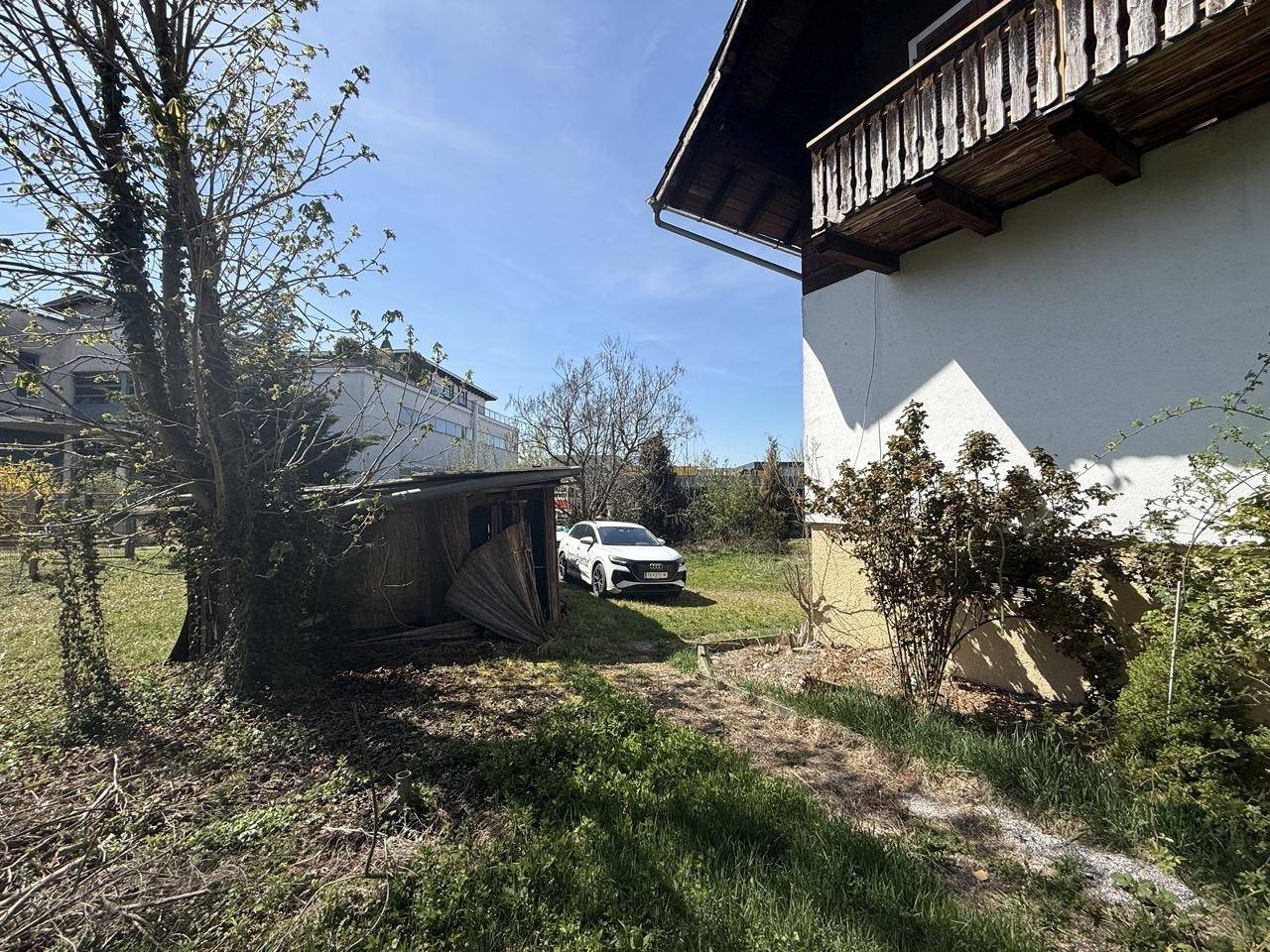 Gartenbereich mit altem Holzschuppen und einem geparkten Fahrzeug auf dem Grundstück.