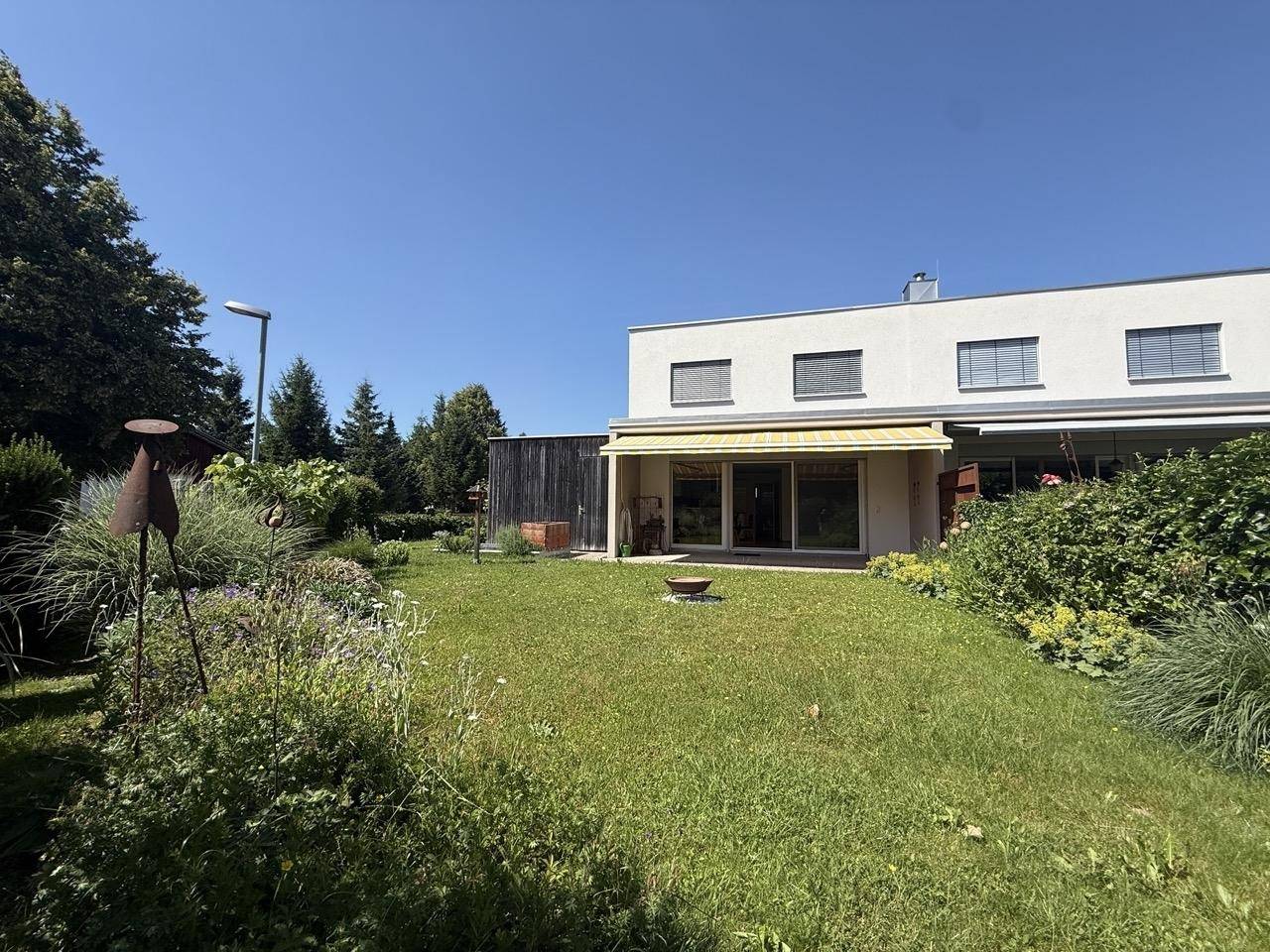 Der sonnige Gartenbereich mit Rasen und einer Terrasse lädt zum Entspannen im Freien ein.