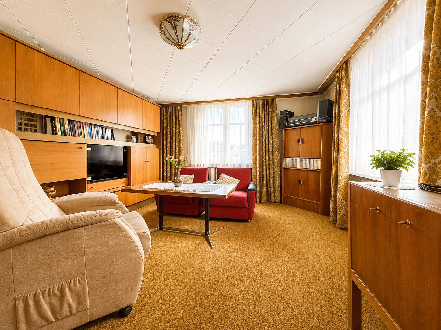 Wohnzimmer im Vintage-Stil mit Teppichboden, Holzmöbeln und rotem Sofa.