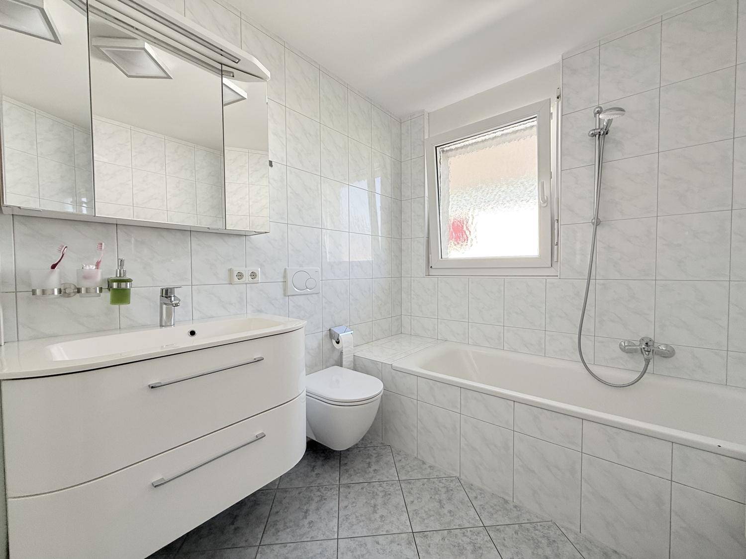 Helles Badezimmer mit Badewanne, WC, Waschbecken und Fenster für natürliche Belüftung.