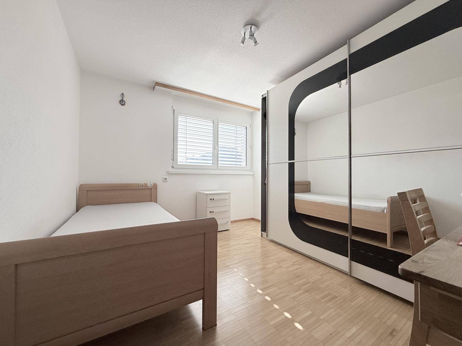Helles Schlafzimmer mit Parkettboden, Einzelbett und großem Spiegelschrank.