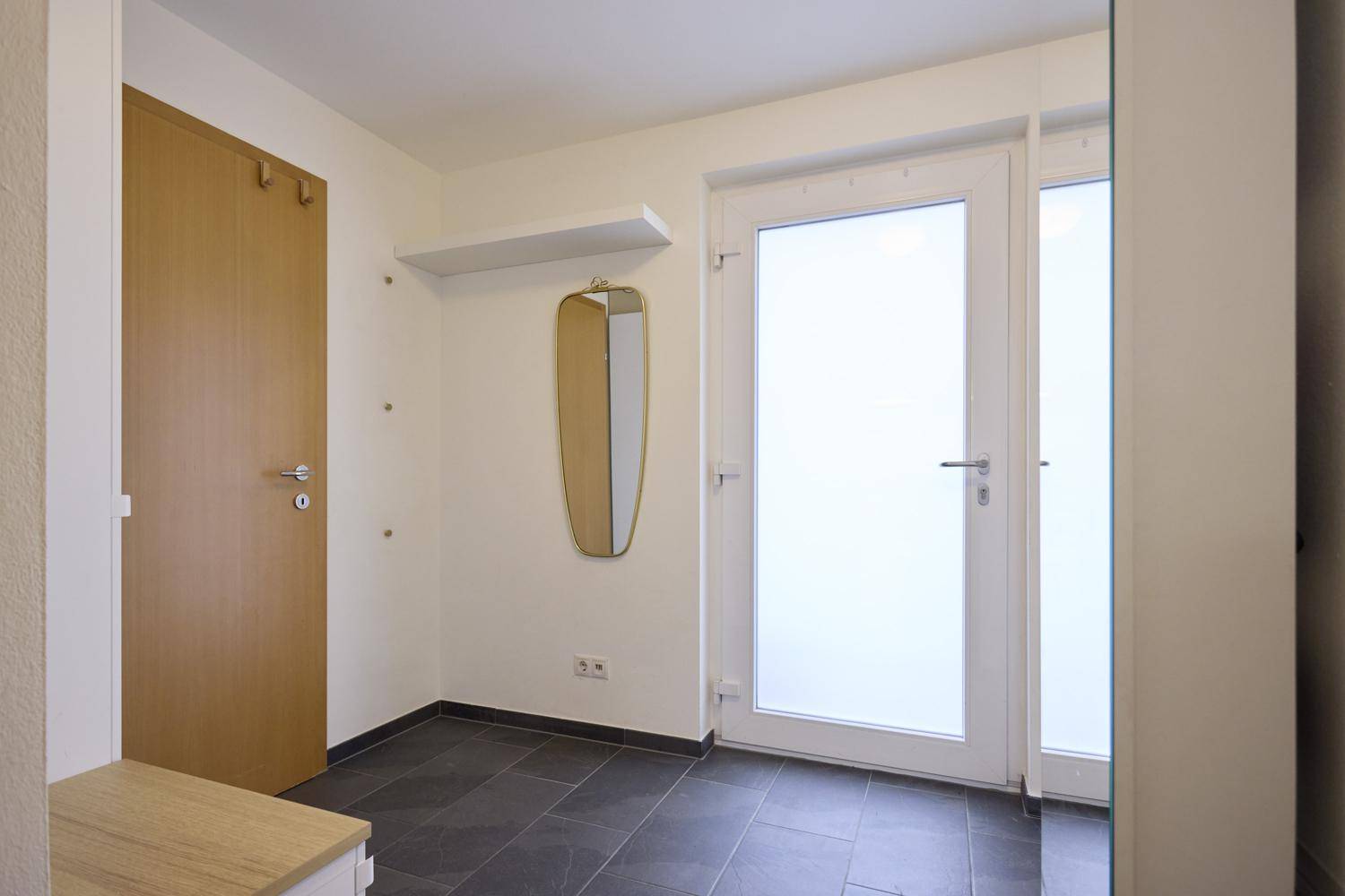 Heller Eingangsbereich mit moderner Garderobe und großem Spiegel.