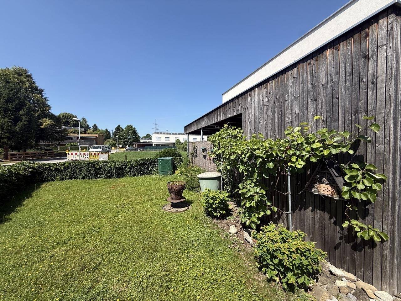 Seitlicher Gartenbereich mit Holzfassade und grüner Hecke, der Privatsphäre bietet.
