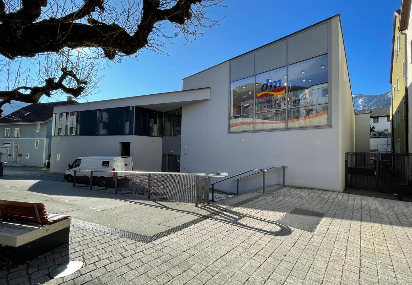 Modernes Gebäude mit Rampe zum Eingang und einem dm-Markt, umgeben von einer gepflasterten Fläche.