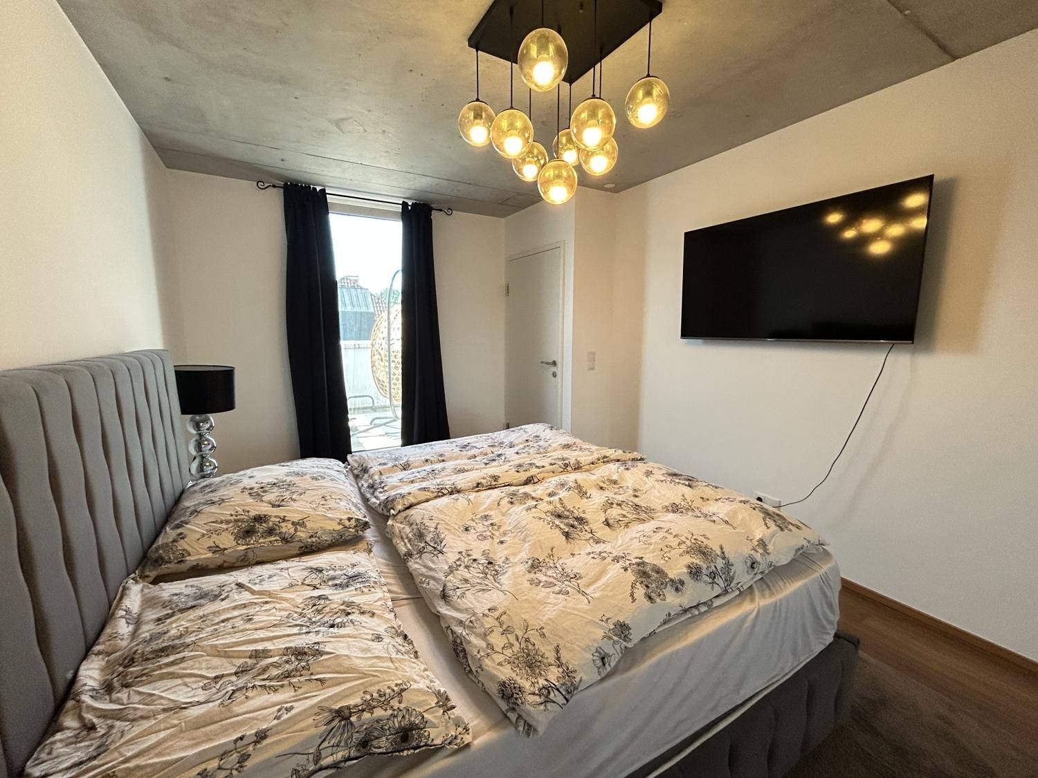 Gemütliches Schlafzimmer mit Doppelbett, Fernseher und Zugang zu einem Balkon.