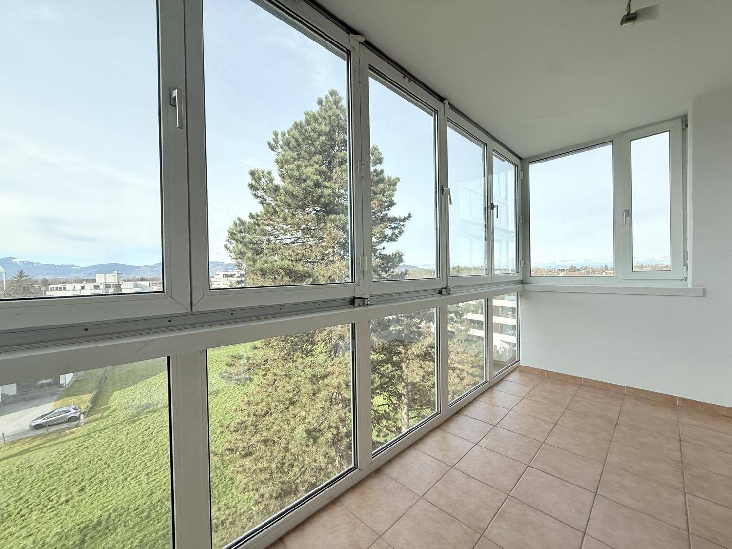 Helle, verglaste Loggia mit Fliesenboden und Panoramablick auf die Umgebung und Berge.
