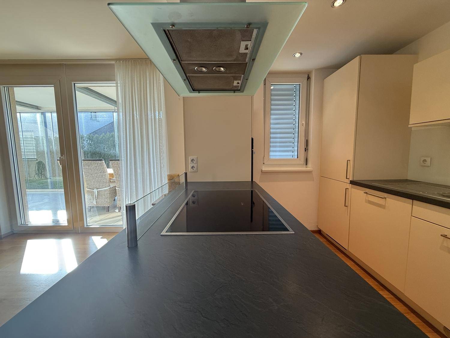 Helle Küche mit Kochinsel, Induktionskochfeld und direktem Zugang zur verglasten Terrasse.
