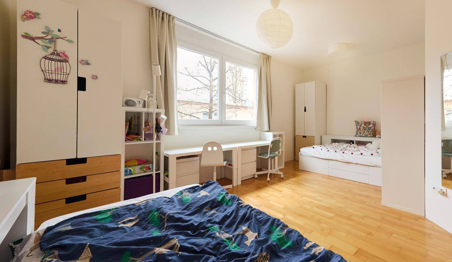 Geräumiges Kinderzimmer mit zwei Betten, Schreibtisch und Holzboden.