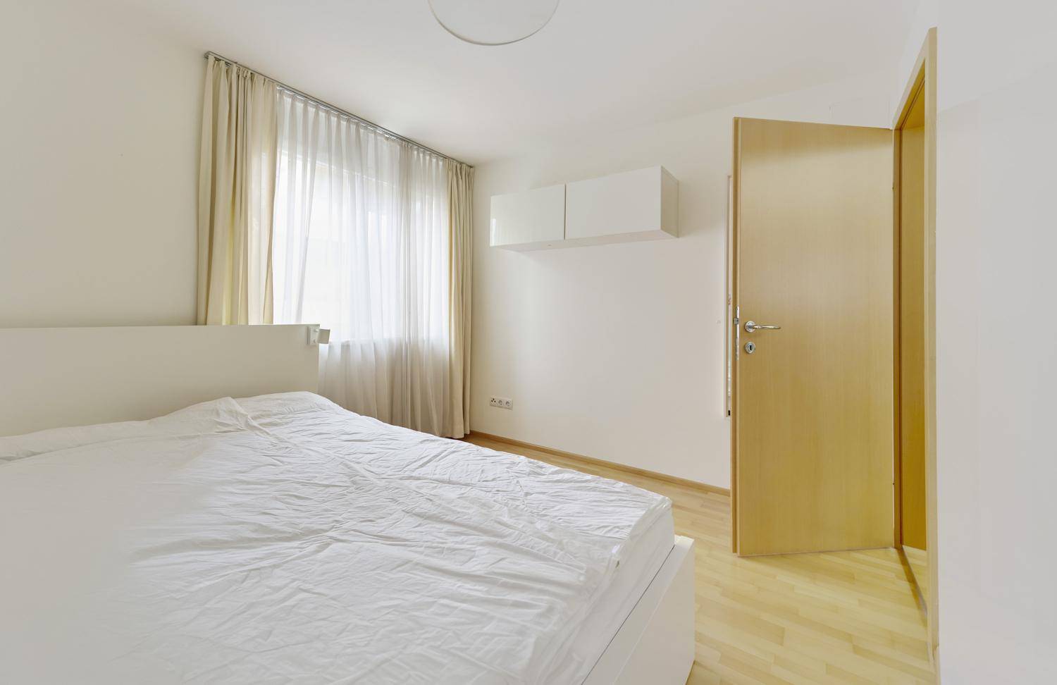Helles Schlafzimmer mit Doppelbett, Holzboden und Fenster.